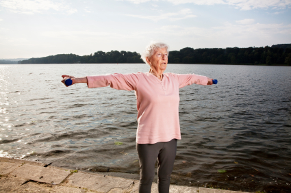 Elderly woman exercises with dumbbells outdoors.