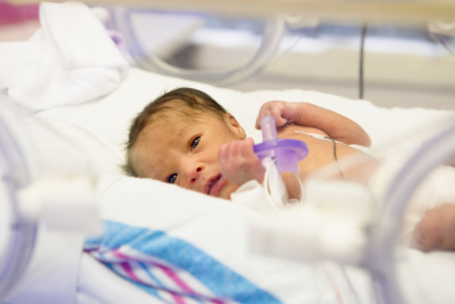 A premature infant looks out from an incubator