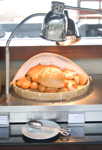 Basket of rolls under lamp, metal tongs in foreground