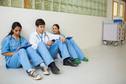 Doctors sitting in a corridor while using smartphones
