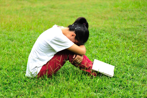 Girl sitting on lawn with her head bowed down