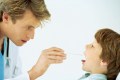 Side view of mid adult doctor examining young boy's (10-11) throat