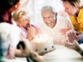 People gathered around senior man blowing out a birthday cake