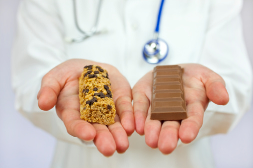 Close up on the hands of a doctor offering the choice of a healthy granola bar or a chocolate bar