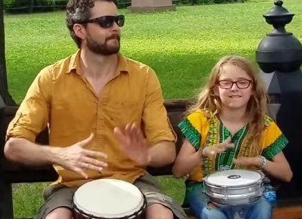 Father and daughter playing hand drum in park