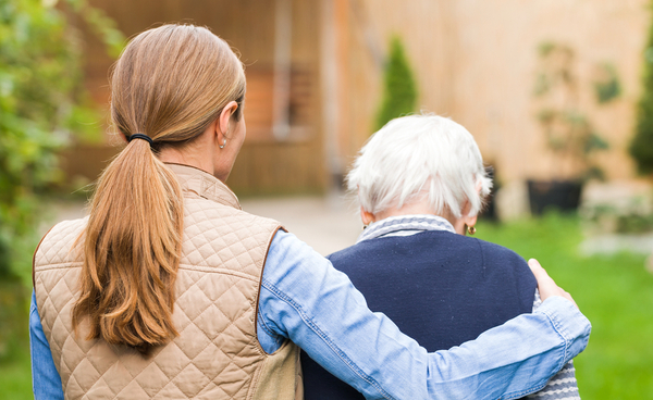 From behind picture of younger woman putting arms around elderly woman