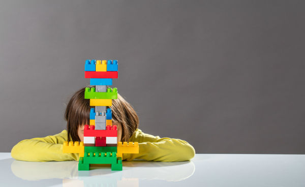 child's face hidden behind colorful toy blocks