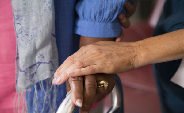 portrait of hands. one hand holding a walker and another on top of that hand in a caring gesture