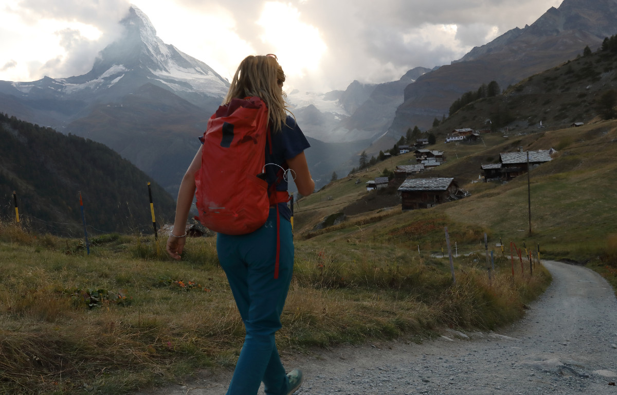 Young woman walking winding road to through small village, mountains in background