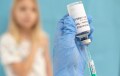 Foreground of hand holding bottle labeled COVID-19 vaccine, with young blond woman in background in soft focus